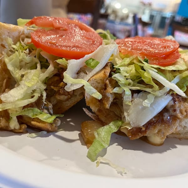 A Stuff'D Steaks & Hoagies cheesesteak, cut in half, topped with fresh lettuce and sliced tomatoes.