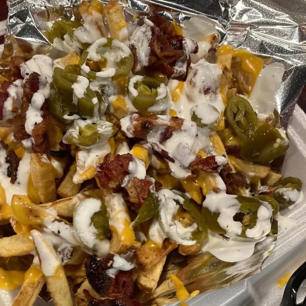 Cheesesteak fries from Stuff'D Steaks & Hoagies, topped with melted cheese, bacon, jalapeños, and white sauce.