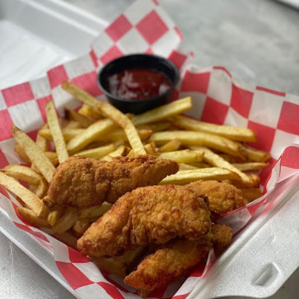 Crispy chicken tenders and golden french fries in a red and white checkered paper tray with ketchup.