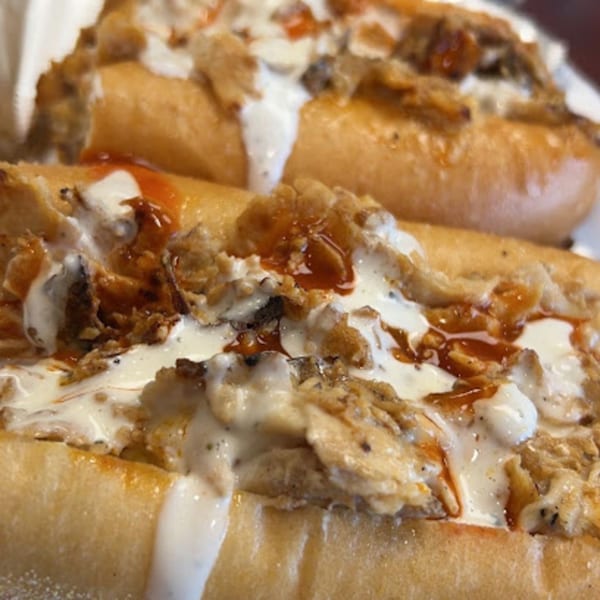 Two Stuff'D Steaks & Hoagies cheesesteaks, generously topped with creamy white sauce and a drizzle of brown sauce.